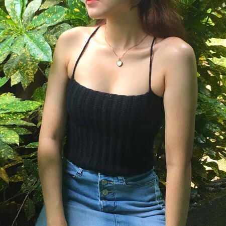 A chic woman wearing a textured black crochet crop top with spaghetti straps, paired with a denim skirt, great for casual wear.